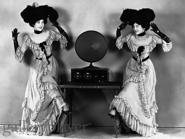 Ladies in long dresses practice polka steps by a radio. ca. 1920s