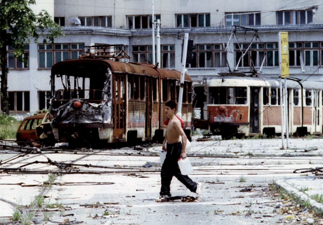 A Bosnian teenager passes throught totaly destrojed trams at the Skenderia square in besiegned Bosni..